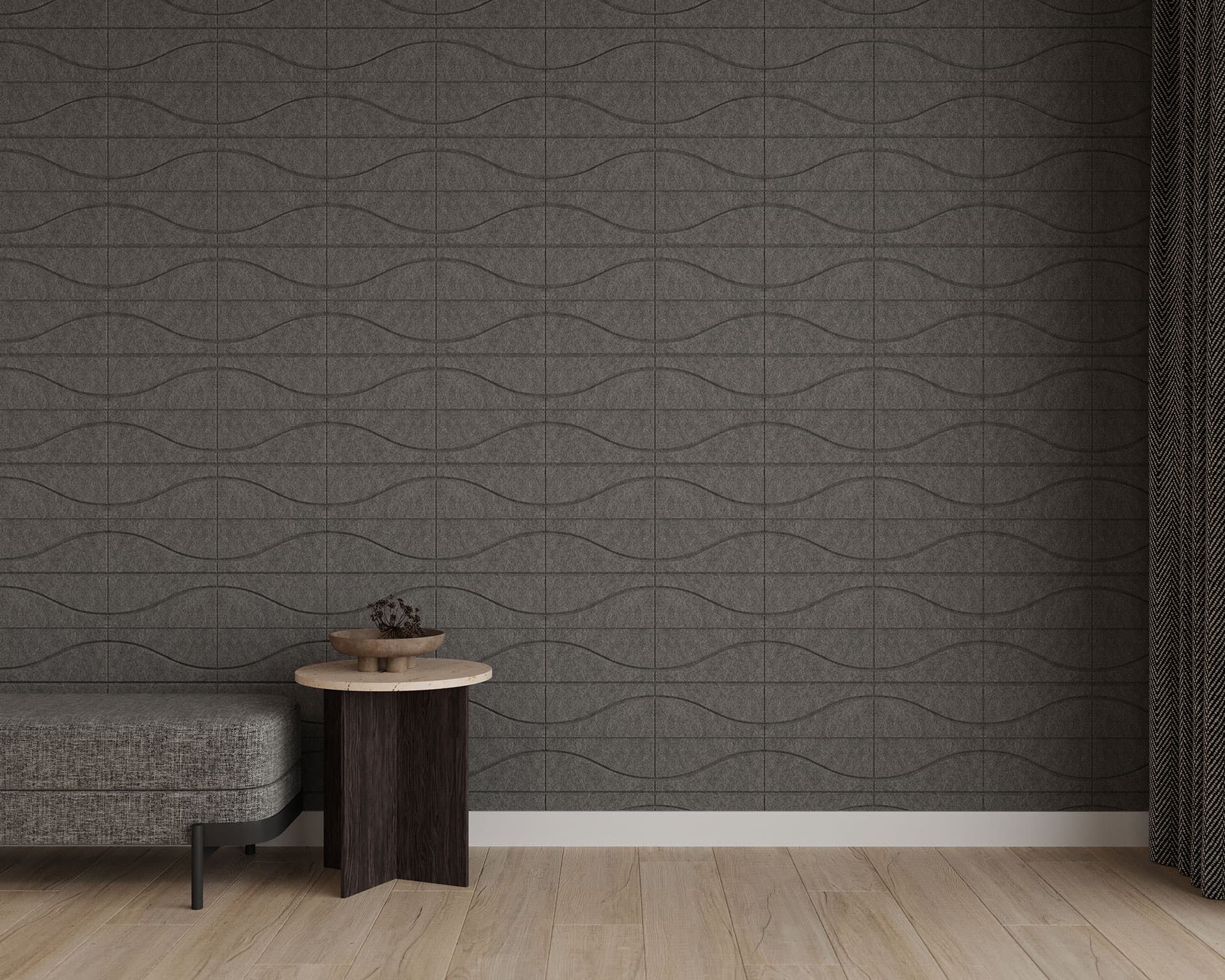 A minimalist room features a gray bench, a small round wooden side table with a plant pot, and dark curtains. The wall has acoustic felt wall tiles in subtle wave patterns of gray tones. The light wood floor enhances the simple and modern atmosphere.