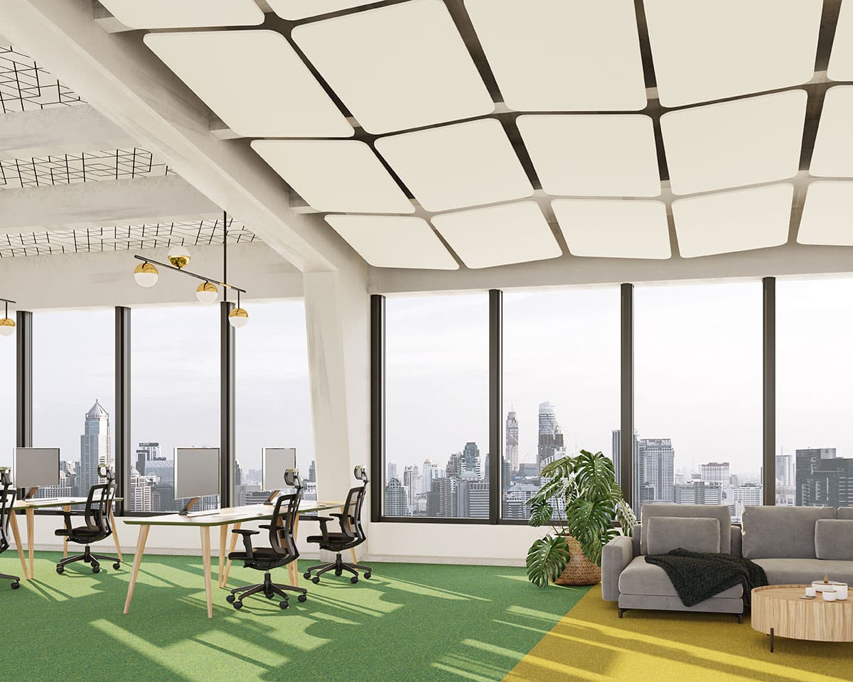 A modern office space with large windows showcasing a city skyline view. The room features workstations with computers and ergonomic chairs. A seating area with a couch and coffee table sits near a plant. The white ceiling, adorned with rectangle acoustic felt ceiling clouds, has a geometric design.