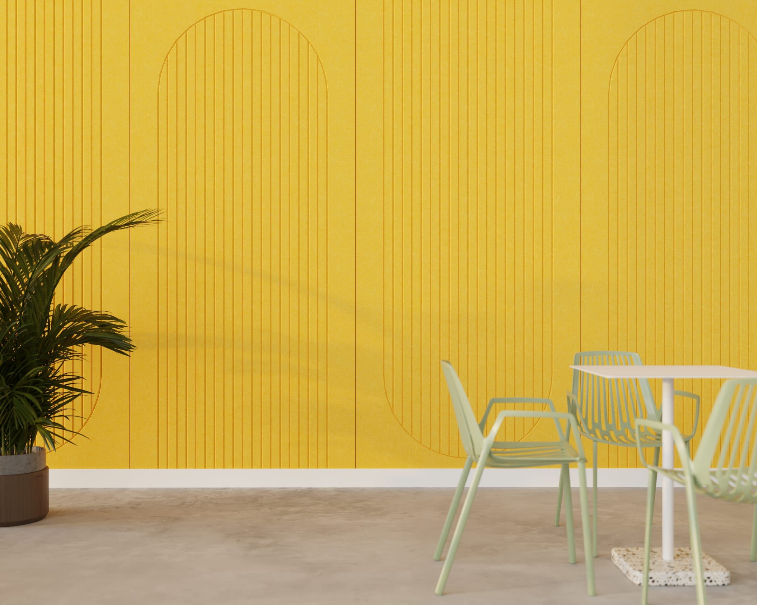 A modern interior with a vibrant yellow wall featuring arched acoustic felt wall panels. There's a potted green plant on the left, and on the right, a white table surrounded by light green chairs on a gray concrete floor. The space is minimalistic and bright.