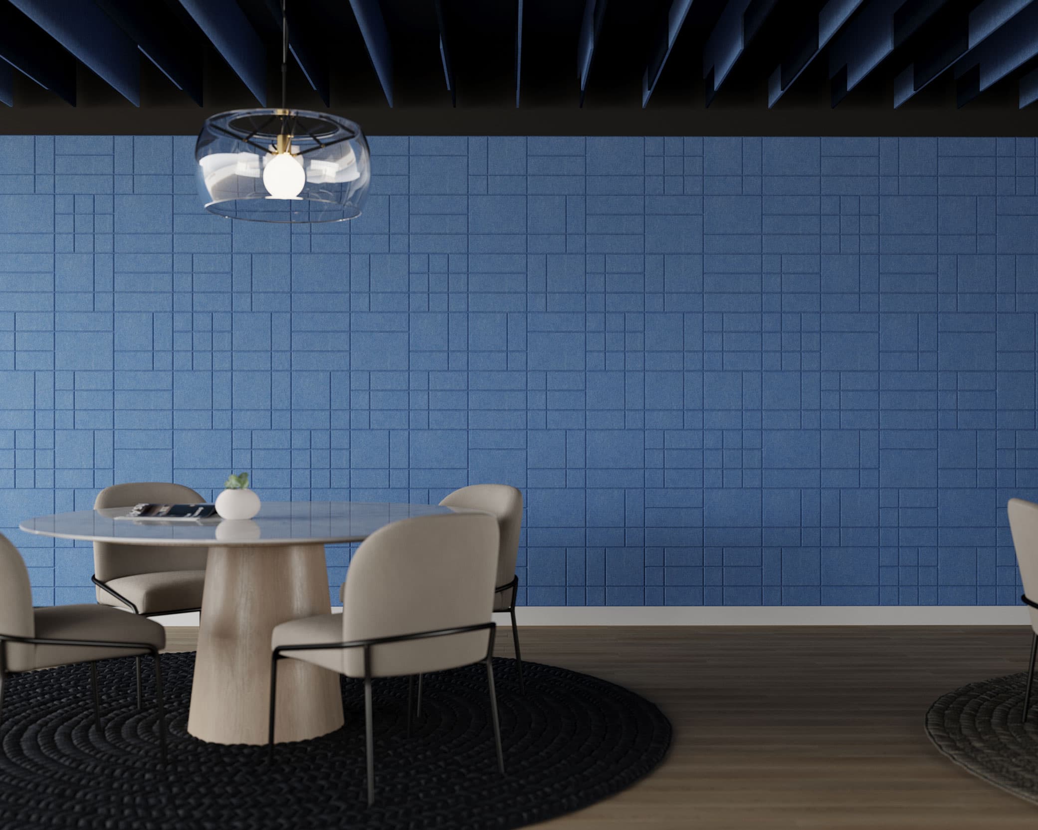A modern conference room featuring a round white table surrounded by beige chairs. The room is adorned with a blue wall with geometric patterns and acoustic felt wall tiles, plus a unique overhead light fixture with a transparent shade. The floor is covered with dark round rugs.