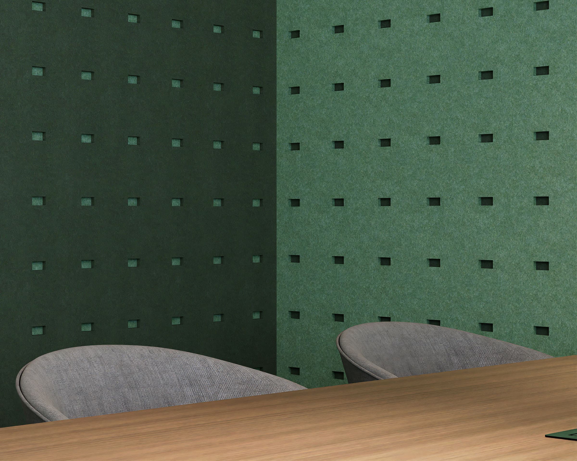 A modern office corner with dark green and light green walls featuring small rectangle cutouts in the acoustic felt wall panels. The room contains a wooden desk and two gray fabric chairs, with the minimalist design focusing on clean lines and a calming color palette.