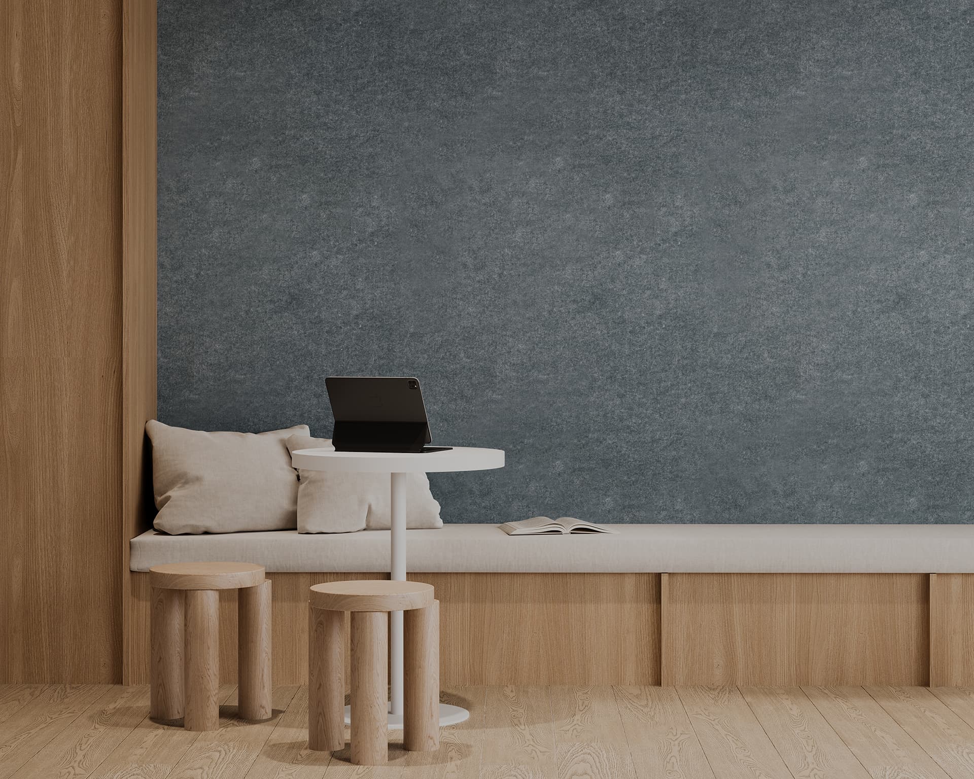 Minimalist room with a wooden bench covered with beige cushions, a small white round table with a laptop, and two wooden stools. A book lies open on the bench. The wall behind is textured in a muted blue-grey acoustic wall panel. The floor has light wooden planks.
