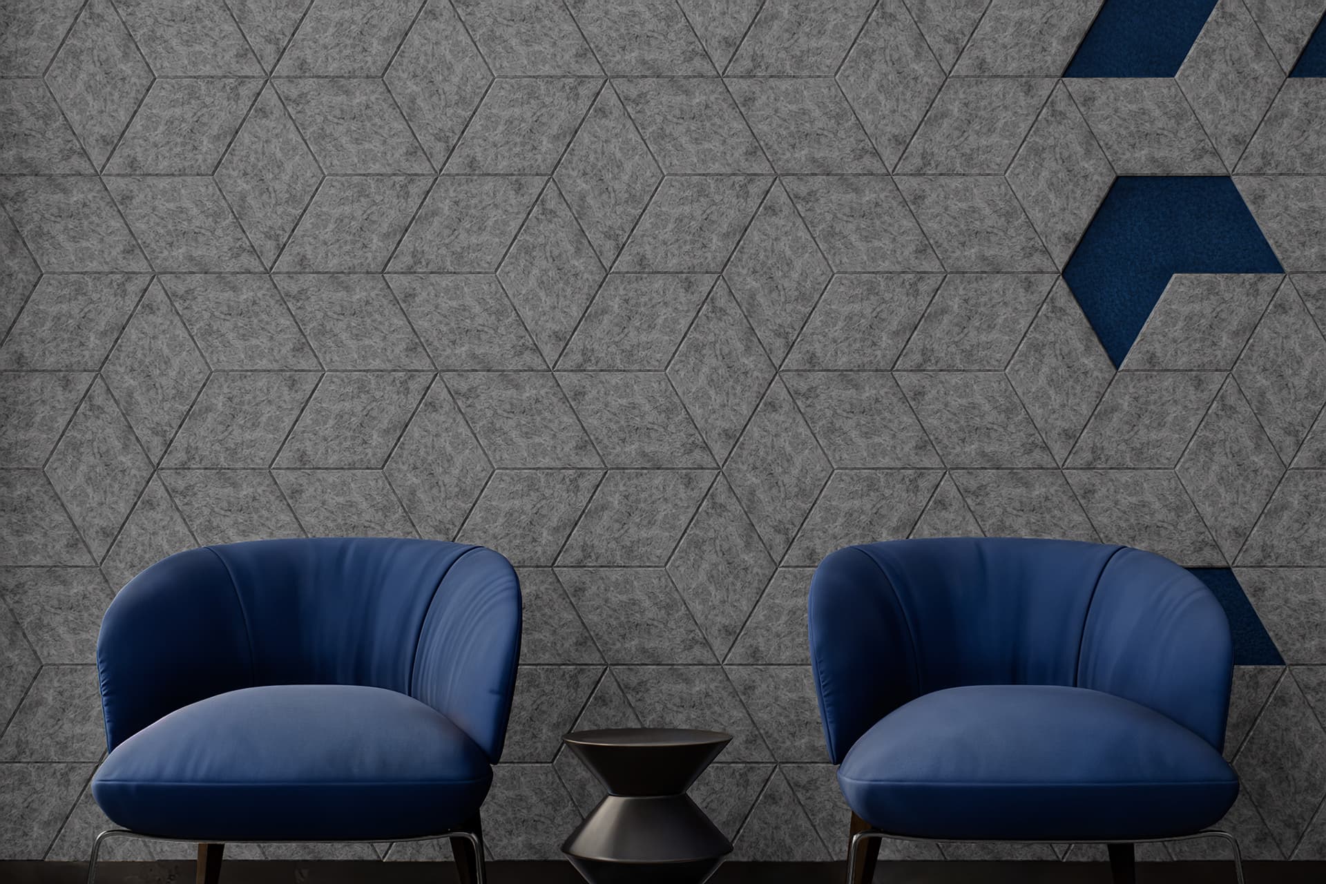 Two blue armchairs sit against a geometric-patterned wall with gray diamond acoustic felt tiles and blue accents. Between the chairs is a small, black, hourglass-shaped side table. The minimalist setting emphasizes the modern and sleek design.