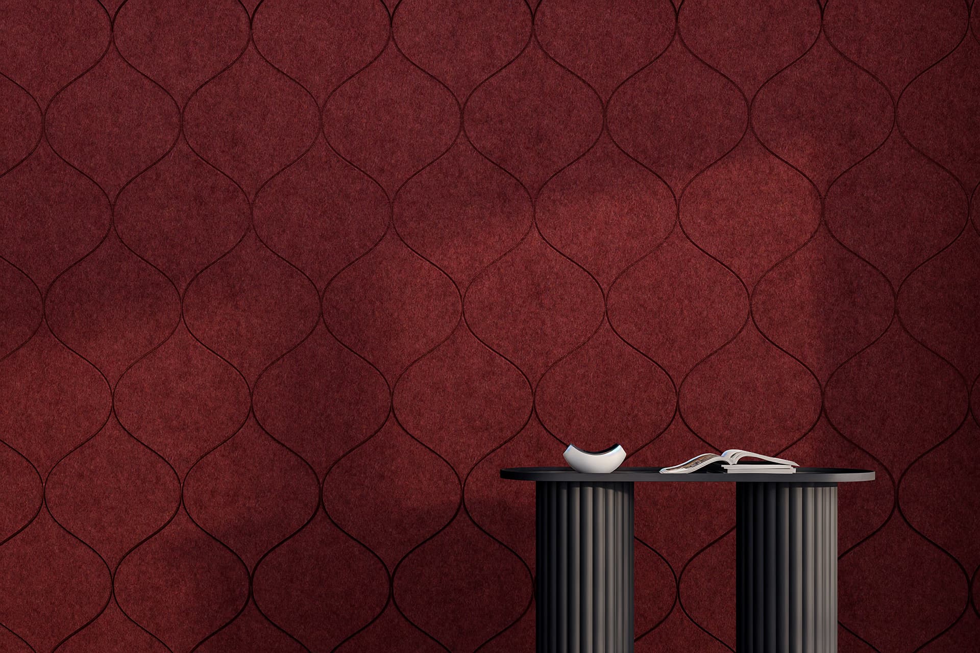 A modern interior scene featuring a textured acoustic felt red wall with a wave-like pattern. In front of the wall, there are two cylindrical black tables. One table has a white ceramic bowl, and the other table has a book opened and facing down. Shadows are cast across the scene.