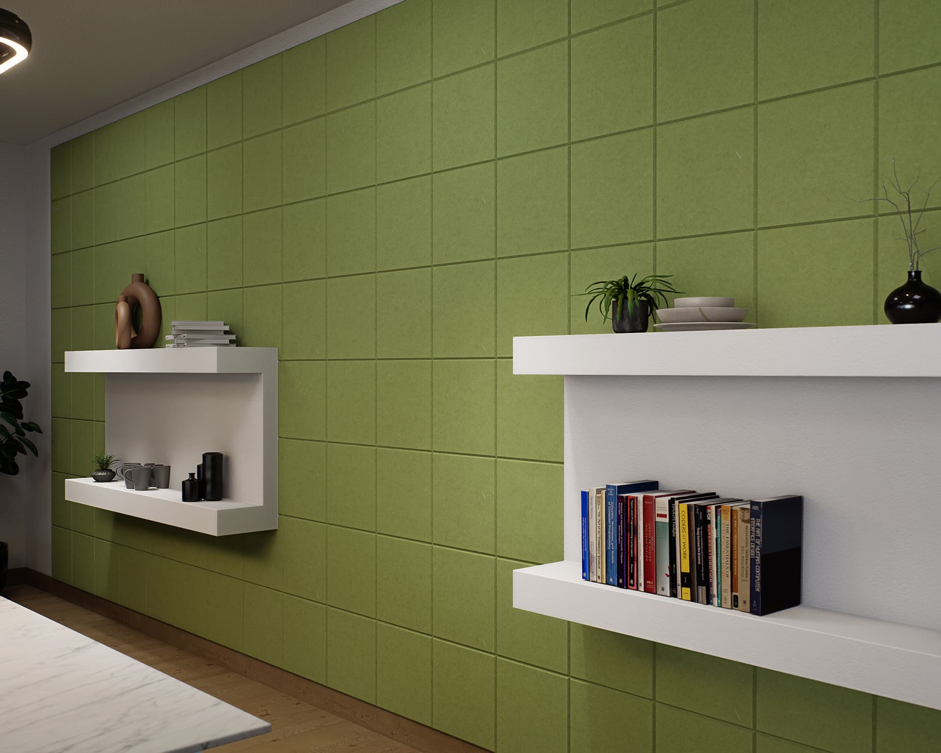 A modern interior with a green acoustic felt tiled accent wall featuring two white floating shelves. The top shelf holds decorative items including plants and vases, while the bottom shelf displays books and additional decorations. A small corner of a white marble table is visible.