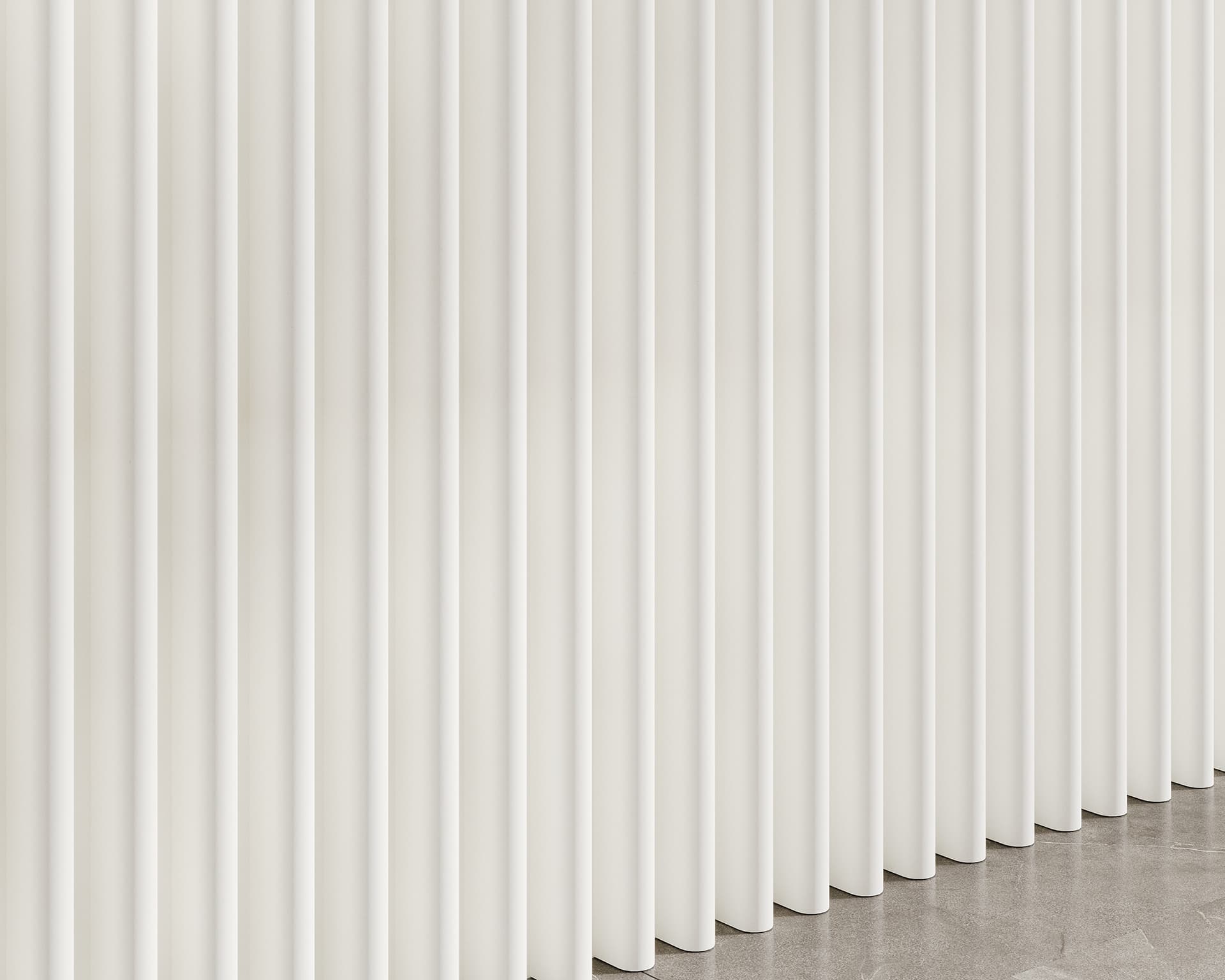 Close-up of a series of tall, vertical white panels made from acoustic felt, creating a modern and minimalist pattern. The panels are evenly spaced and extend for the full height of the image, casting subtle shadows on the floor below.