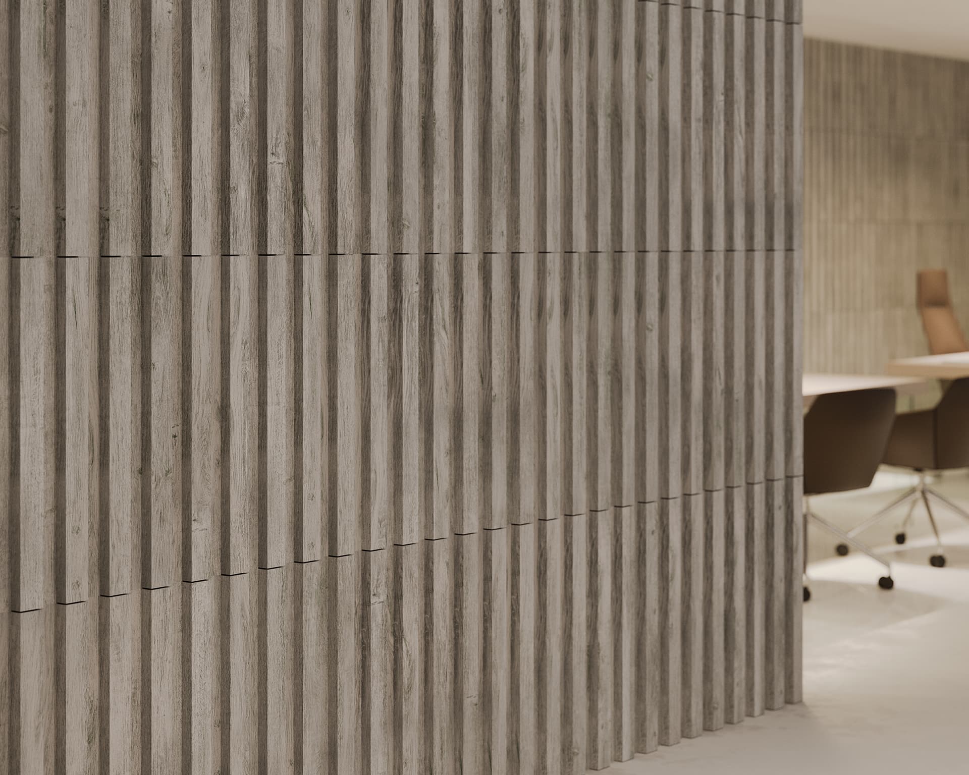 The textured, modern wall features acoustic felt panels with a subtle woodgrain finish, extending into an office space. Partially visible office furniture includes brown chairs on wheels and a white table. The room maintains a clean, minimalist design while enhancing sound quality.