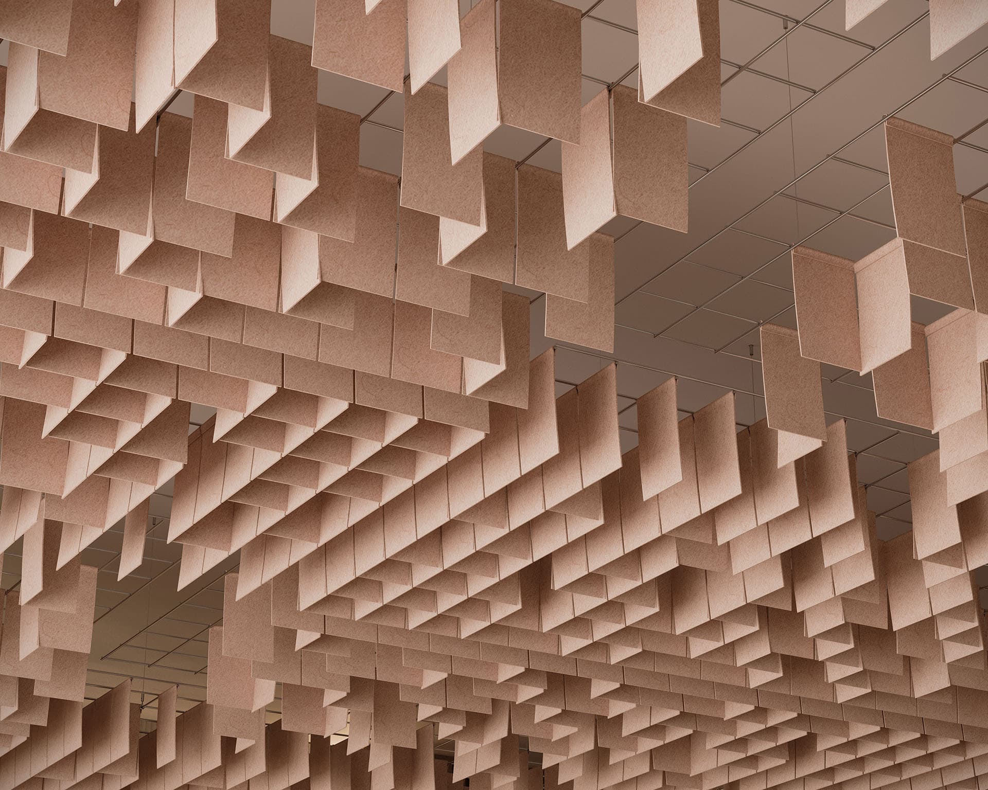 The ceiling features numerous hanging rectangular panels of acoustic felt, arranged in an artistic pattern like floating clouds. These light brown elements create an abstract geometric design, enhancing the architectural interest of the space with their natural charm.