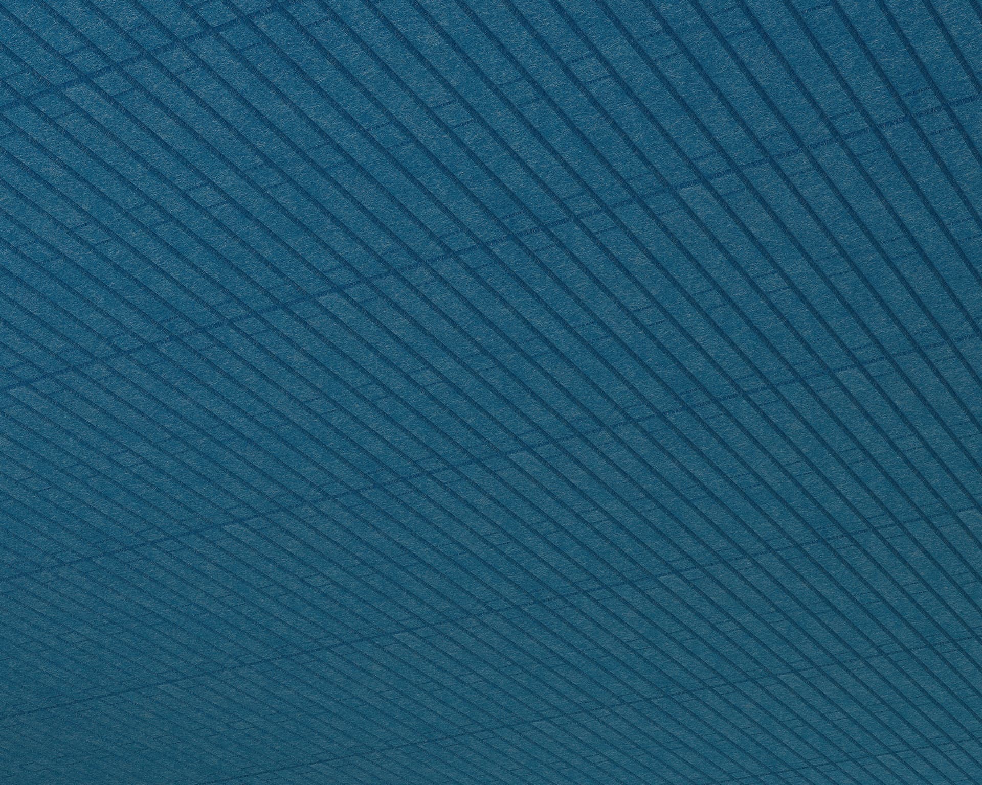 A close-up view of an acoustic felt textured surface with parallel, diagonal lines forming a grid-like pattern. The blue-toned design evokes the cozy tranquility of a cabin, as light and shadow play across its surface, adding depth and dimension.