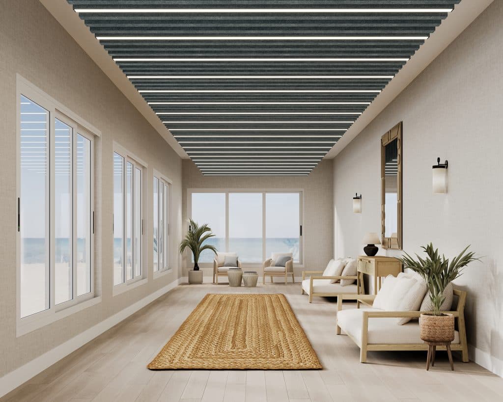 A modern, minimalist living room with large windows showcasing an ocean view. The space features light-colored sofas, a wooden console table, and indoor plants. The ceiling has dark acoustic felt baffles, and a woven rug runs along the light wood floor.